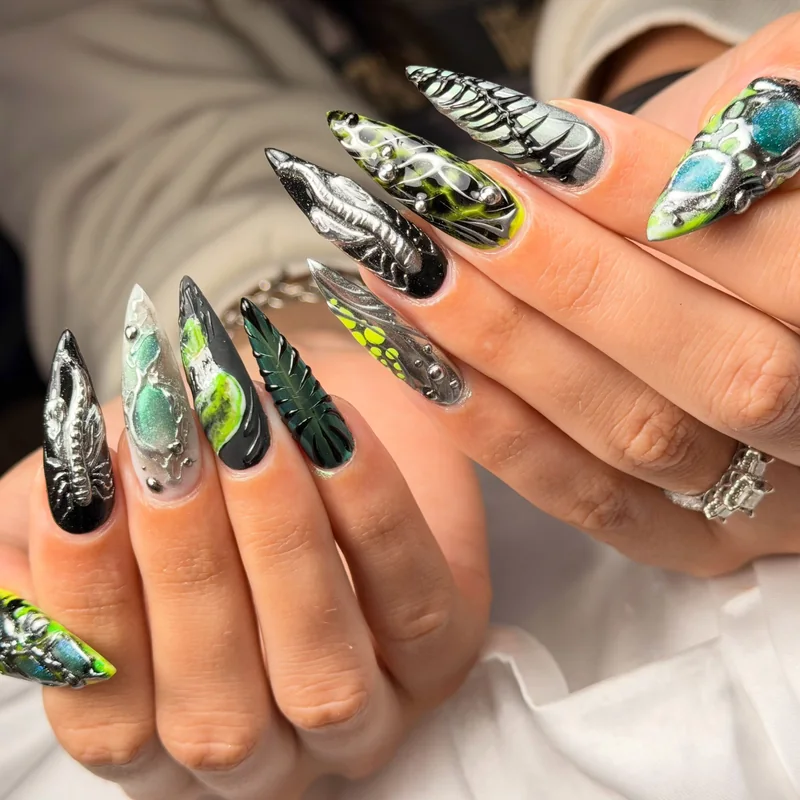 Long almond nails with silver sculptural patterns, translucent green accents, and turquoise gemstone-like details.