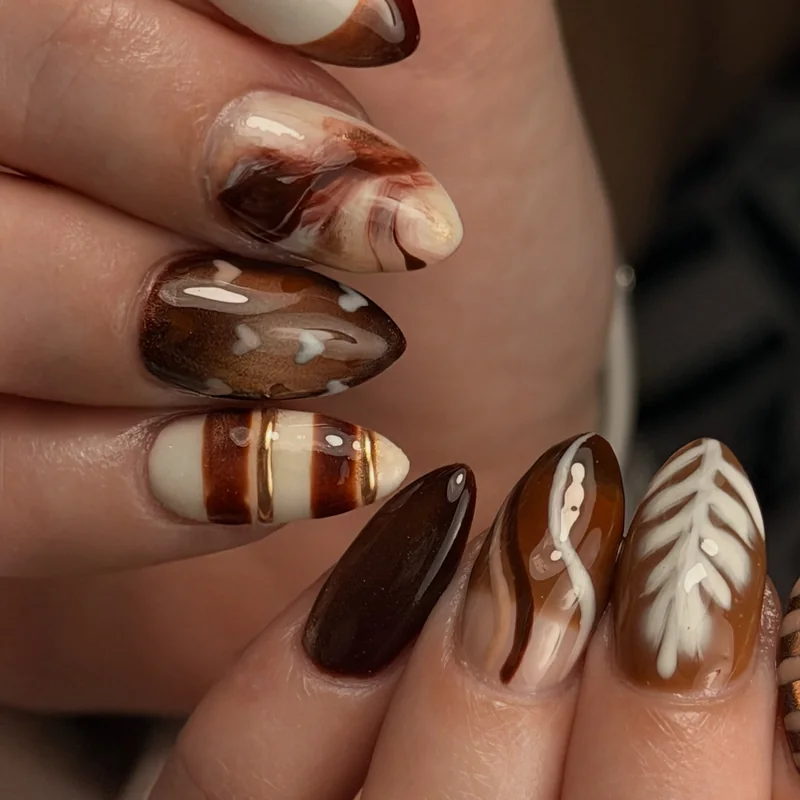 Almond nails in chocolate, cream, and caramel with latte-style swirls, stripes, and abstract marbling.