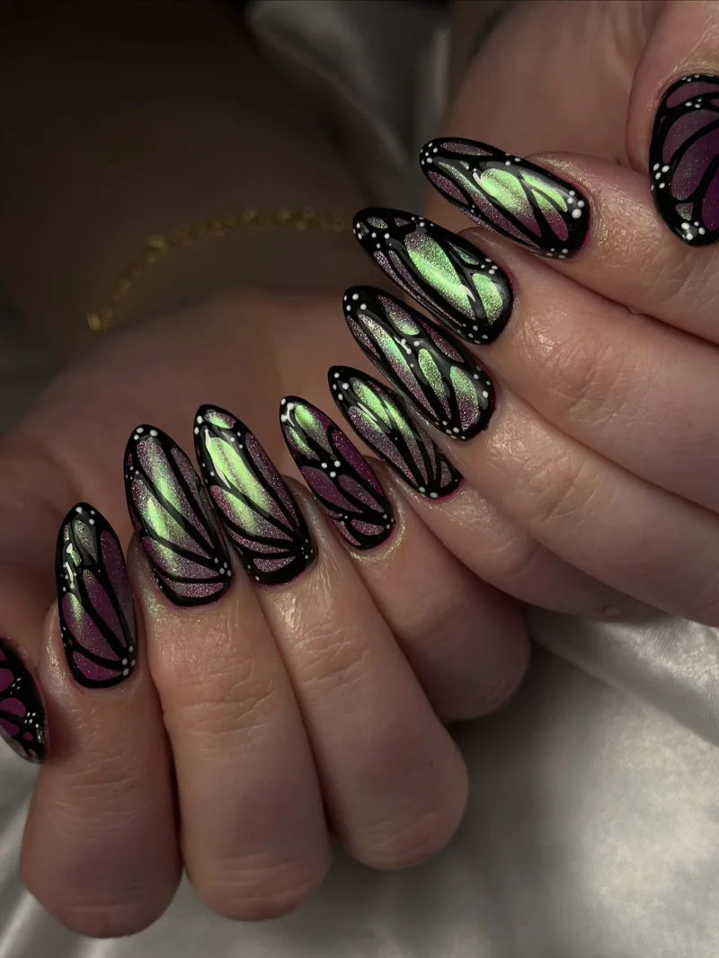 Almond nails with green and violet iridescent shimmer outlined in delicate black butterfly-wing patterns.