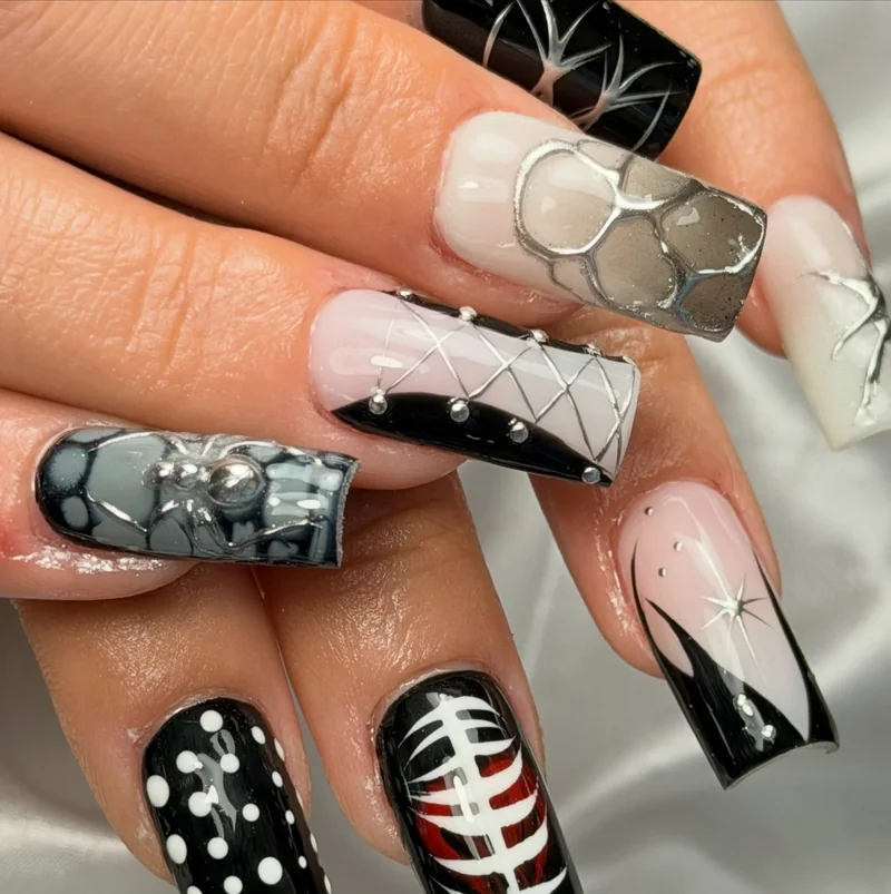 Long square nails with black, white, and silver patterns, including a web, corset lacing, and rib cage art.