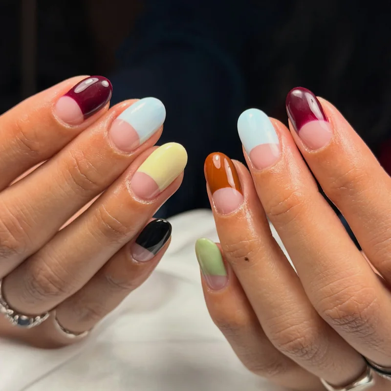 Rounded nails with burgundy, blue, yellow, green, and amber French tips on a sheer pink base.